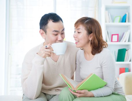 Asian couple reading booking and drinking tea/coffee at home