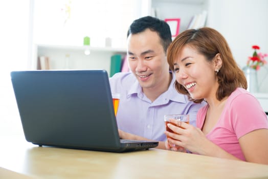 Asian couple using notebook and drinking tea / coffee at home