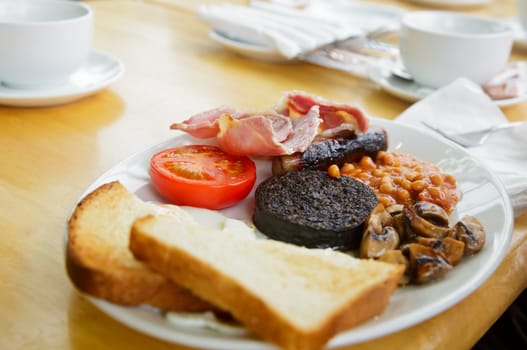 Plate with Full Scottish breakfast containing toasts, fried eggs, baked beans, grilled black pudding, sausage, tomato, mushrooms and bacon