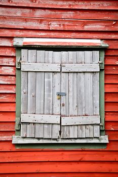 Old weathered wooden shuttered window on a red wall locked