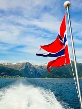 Fluttering Flag of Norwegian Post against plenty stern wave of cruise ship at fjord