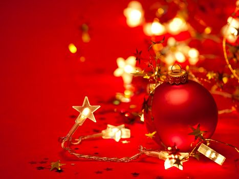 Red Christmas bauble with star-shaped lights and tinsel on red background, shallow DOF