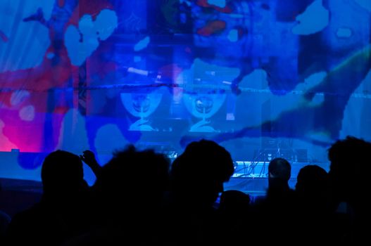 Silhouettes dancing in a club set against a blue backdrop.