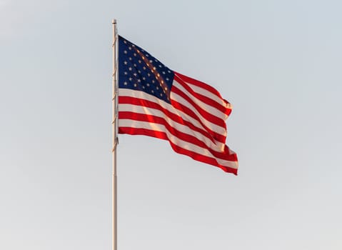 The US American red, white and blue flag flying in front of a blue cloudy sky.