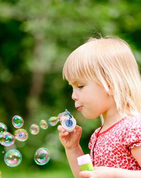 Cute little girl making soap bubbles outdoors