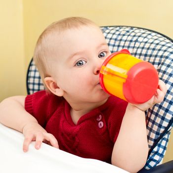 Little baby girl sitting in a highchair with plastic drinking cup
