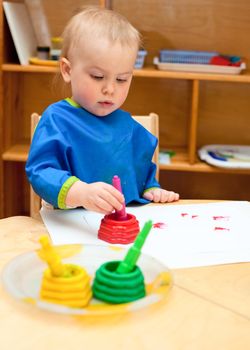 Little girl wearing blue apron painting with watercolors