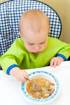 Little baby girl eating with spoon in a highchair