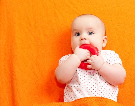 Little baby girl with teething toy on orange backgroung