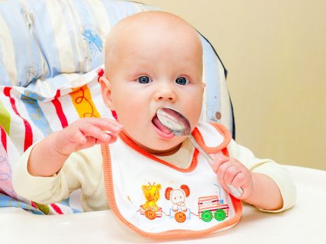Little baby girl sitting in highchair with spoon