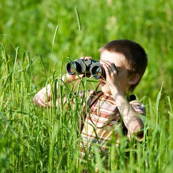 Young boy in a field looking through binoculars