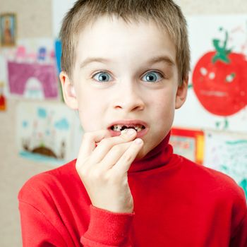 Boy holding lost deciduous teeth against his drawing on the wall