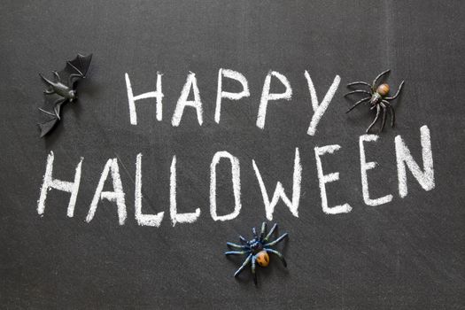 Happy Halloween message handwritten on blackboard with spiders around