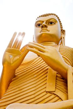 The giant Golden Sitting Buddha statue on roof of the Golden Temple in Dambulla, Sri Lanka, with sun shining through his fingers