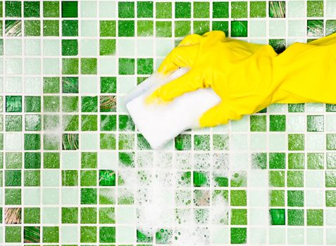 Hand in yellow protective glove cleaning mosaic wall