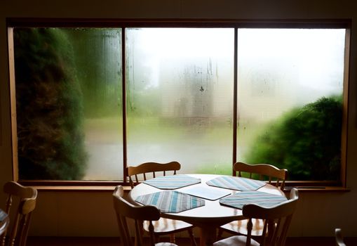 Empty table and chairs against misted window at casual bistro