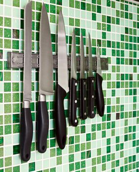 Kitchen knives on green mosaic wall