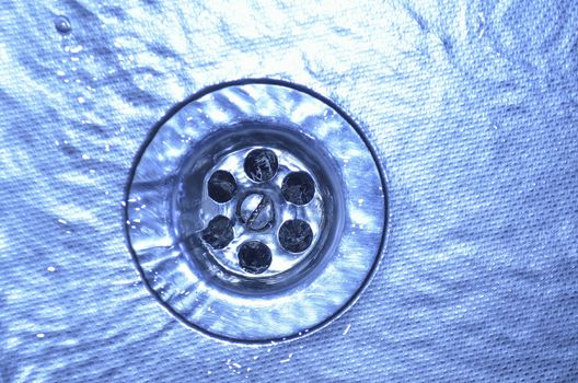 flowing water on metallic sink and drain hole close-up; focus on drain holes