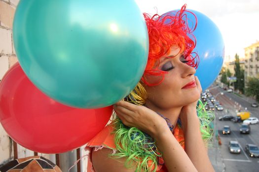 Beautiful dreaming girl with closed eyes in multicolor wig and balloons dreaming looking over the city