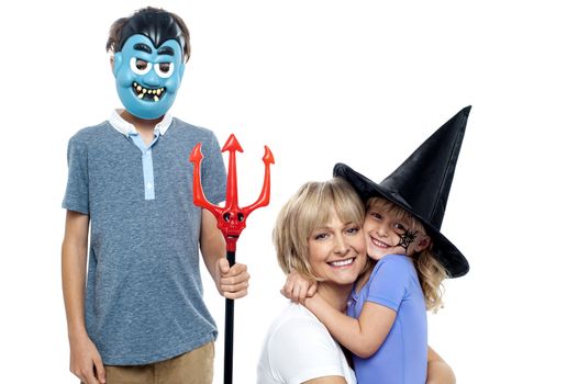 Mother hugging her daughter in witches hat while son wearing dracula face mask and holding pitchfork.