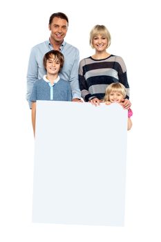 Smiling family of four standing behind a blank whiteboard.