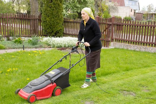 old woman mowing grass with an electric mower