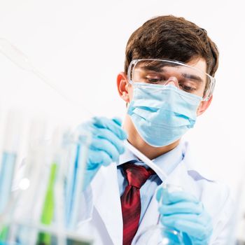 scientist working in the lab, in protective mask, examines a test tube with liquid