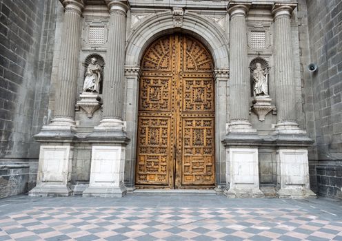 Wooden entrance doors to The Metropolitan Cathedral of the Assumption of Mary of Mexico City. It  is the oldest and largest cathedral in the Americas and seat of the Roman Catholic Archdiocese of Mexico. It is situated atop the former Aztec sacred precinct near the Templo Mayor on the northern side of the Plaza de la Constitución in downtown Mexico City. The cathedral was built in sections from 1573 to 1813 around the original church that was constructed soon after the Spanish conquest of Tenochtitlán, eventually replacing it entirely. Spanish architect Claudio de Arciniega planned the construction, drawing inspiration from Gothic cathedrals in Spain.
