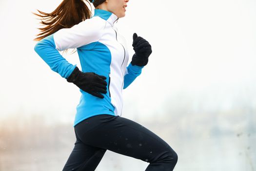 Running athlete woman sprinting during winter training outside in cold snow weather. Close up showing speed and movement.