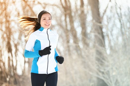 Running sport woman. Female runner jogging in cold winter forest wearing warm sporty running clothing and gloves. Beautiful fit Asian / Caucasian female fitness model.