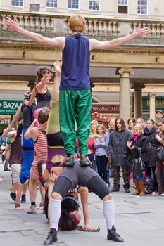 BATH, ENGLAND - MAY 14: A troupe of acrobats performs for spectators outside the Pump Rooms in Bath, England on May 14, 2010. Adjacent also to Bath Abbey, this is the main site for the many street entertainers in this tourist city