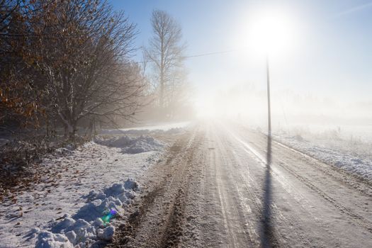 Winter fog road with powerline post and direct sun