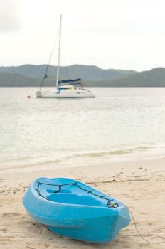 Blue canoe on beach with sailboat on background