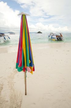Unused beach umbrella on the beach with speed boat on background