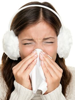Flu or cold - sneezing woman sick blowing nose. Young woman being cold wearing earmuffs and sweater. Asian Caucasian female model.