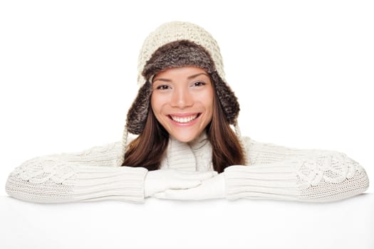 Winter woman sign banner. Cute smiling woman in warm winter sweater and wool cap showing blank white paper poster isolated on white background.