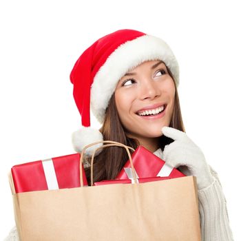 Christmas shopping woman thinking wearing santa hat and holding christmas gifts in shopping bag. Thinking mixed race Chinese Asian / Caucasian female model looking sideways smiling happy isolated on white background.