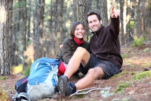 Young happy couple hiking in forest. Smiling couple resting enjoying a break during hike vacations. Caucasian man model. Asian woman model.