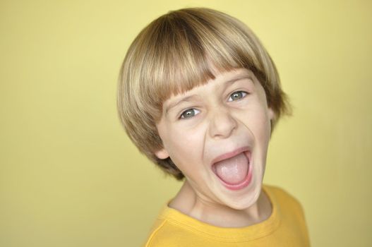 Closeup of young blonde boy screaming on yellow background