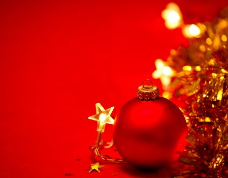 Red Christmas bauble with star-shaped lights and tinsel on red background, shallow DOF