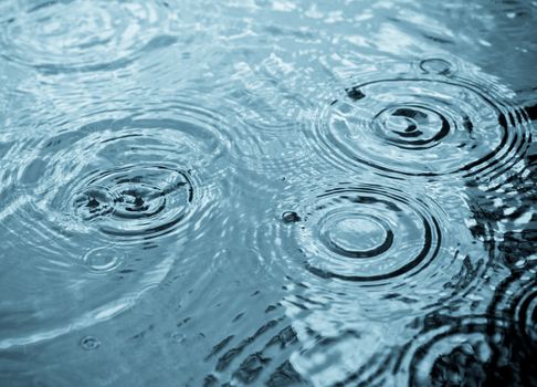 Rain drops rippling in a puddle with blue sky reflection