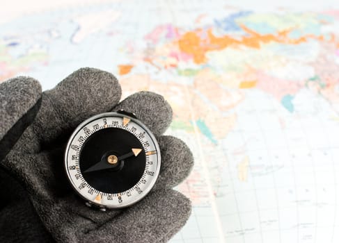 Hand in hiking glove holding compass with map of the world in background