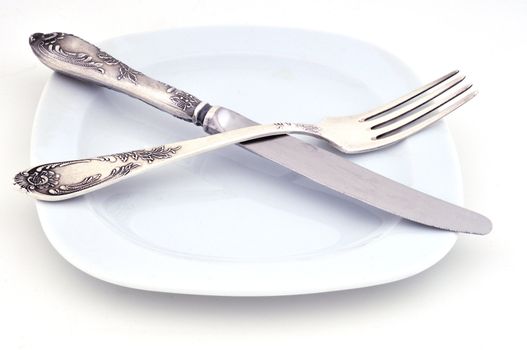 Knife and fork are on a white plate against a white background