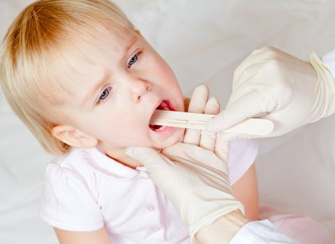 Pediatrician examining little girl's throat with tongue depressor