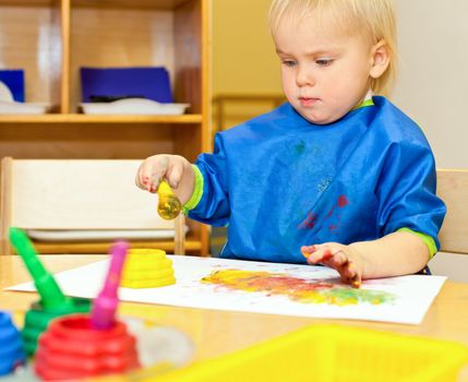 Little girl wearing blue apron painting with watercolors