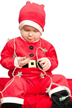 Little baby girl wearing Santa Claus costume playing with christmas lights on white background