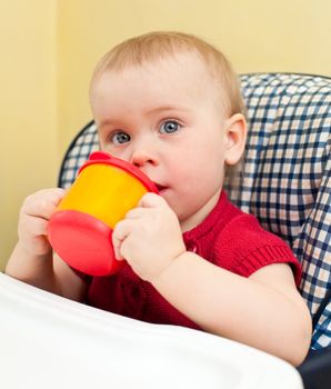 Little baby girl sitting in a highchair with plastic drinking cup