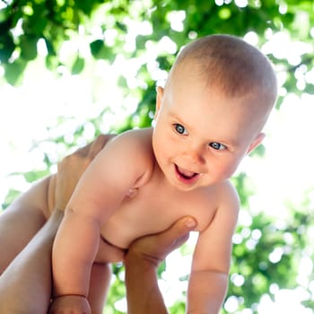 Mother holding her child against sunny leaves, shallow DOF