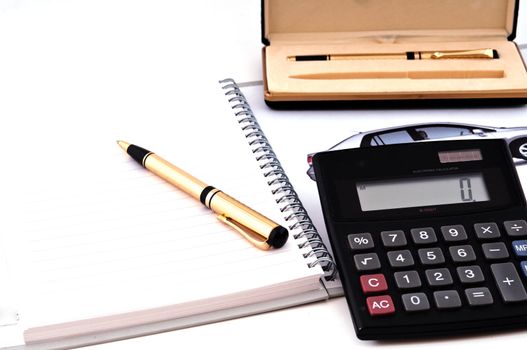 Open notebook, pen and calculator photographed close-up against a white background