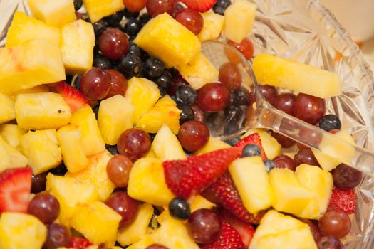 Large bowl of colorful fruit salad containing pineapples, strawberrys, grapes.